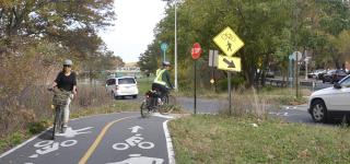 Two cyclists ride on painted separated bike lanes by Pelham Parkway in the Bronx.